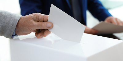 Eine Hand wirft einen Stimmzettel in eine Wahlurne.