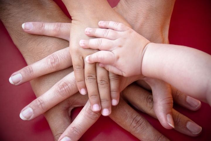 Vier aufeinander gelegte Hände von Erwachsenen und Kindern.