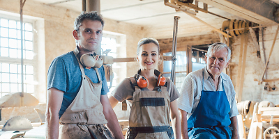 3 Personen in Arbeitskleidung lehnen sich am Arbeitsplatz an einen Tisch