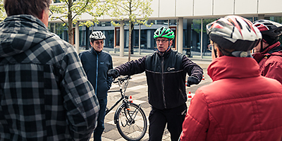 Ein Mann mit Fahrradhelm steht gestikulierend vor einer Gruppe Personen.