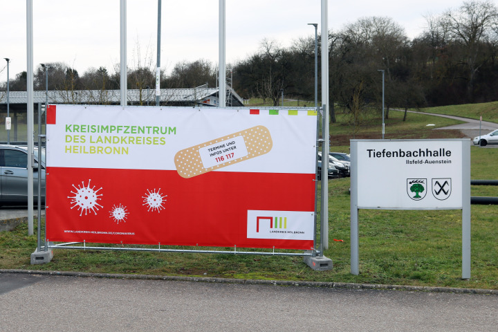 Ein Bauzaunbanner steht vor dem Kreisimpfzentrum in der Tiefenbachhalle in Ilsfeld-Auenstein.