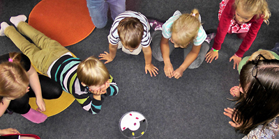 Kleine Kinder liegen im Kreis auf dem Boden und spielen ein Spiel.